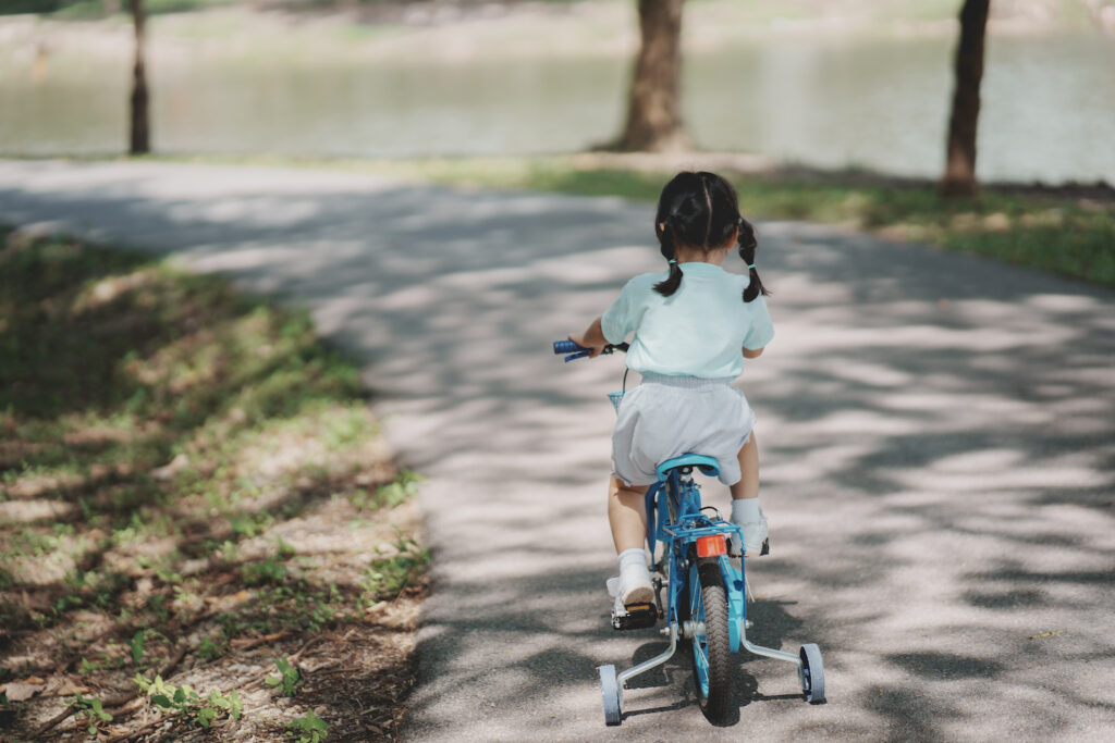 Asian baby girl child learning to ride bicycle in the park garden. Education concept for kid practiice cycling at park, baby sport concept.